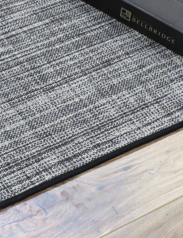 Linen rug, Color: Charcoal 31 / 5700 showing serged edge. Linen rug, Color: Charcoal 31 / 5700 Image shows serged edges of rug with Bellbridge architect folder as prop. Linen Charcoal has two yarn colors (charcoal and white) woven to mimic the texture and look of linen.