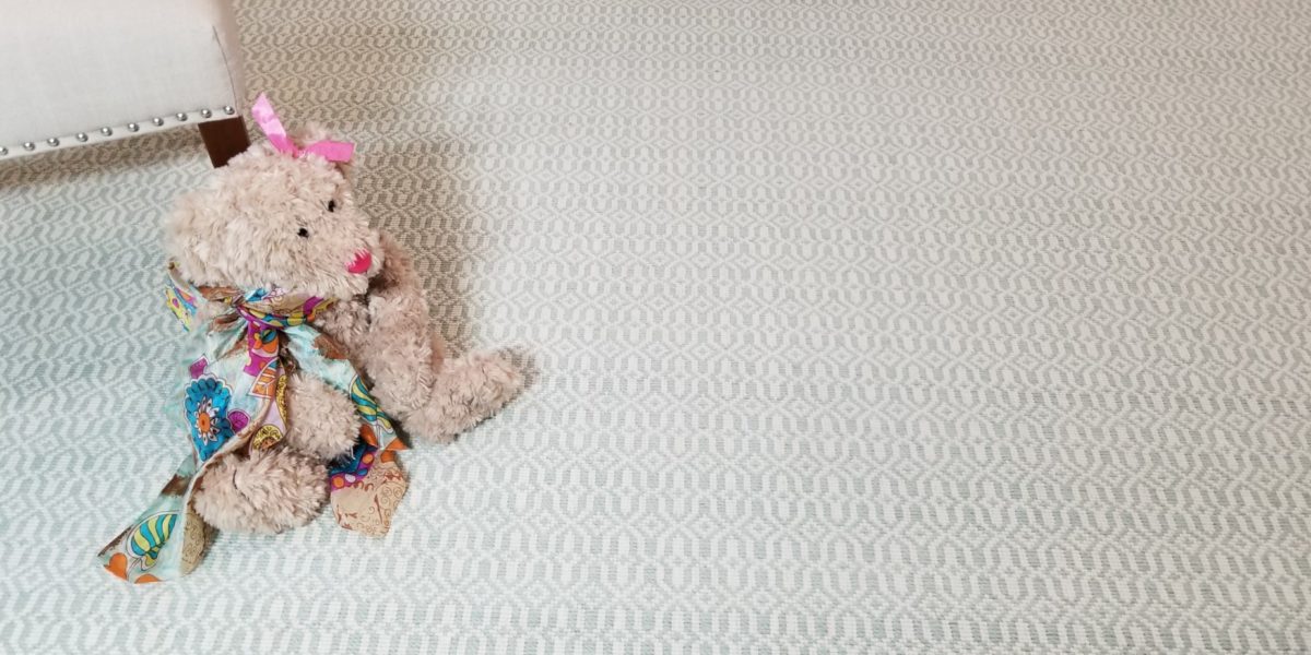 Mosaic , Color: Lt Green 620/1515 shown with toy stuffed bear against chair leg used as props. Mosaic is a loop pile, handloomed with 2 yarn colors (lt green/white) creating a motif that resemble mosaic tiles.
