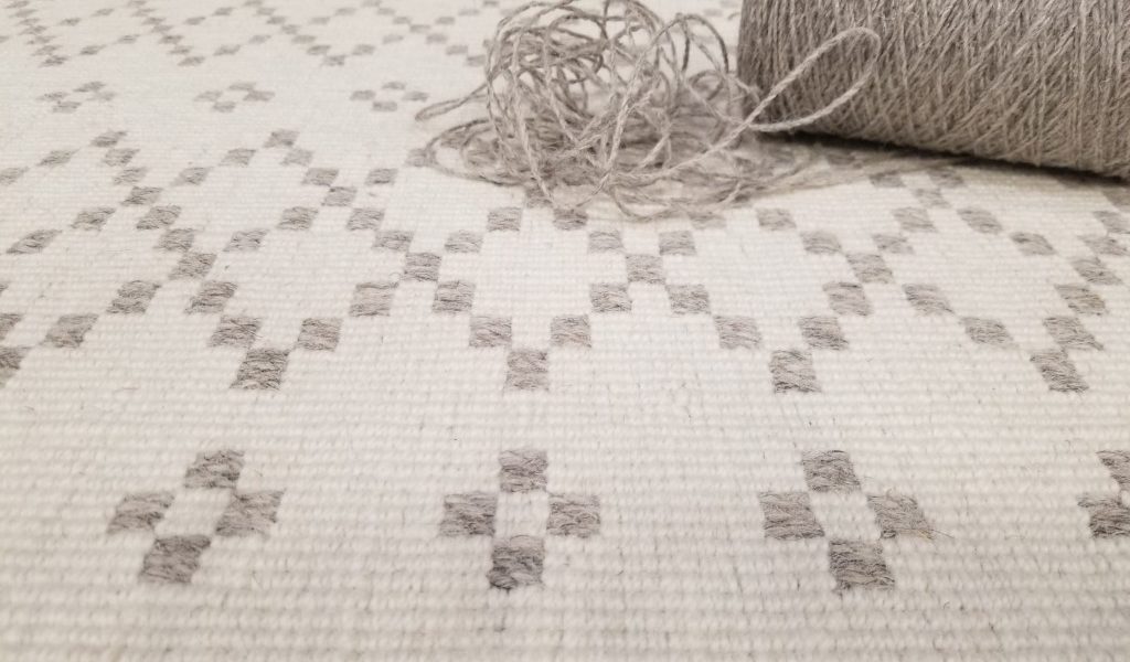 Skyline, Color: Ivory/Grey 720/1508 shown with spool of grey yarn as used in fabrication of carpet. Skyline is a loop pile with diamond motifs going across the width.