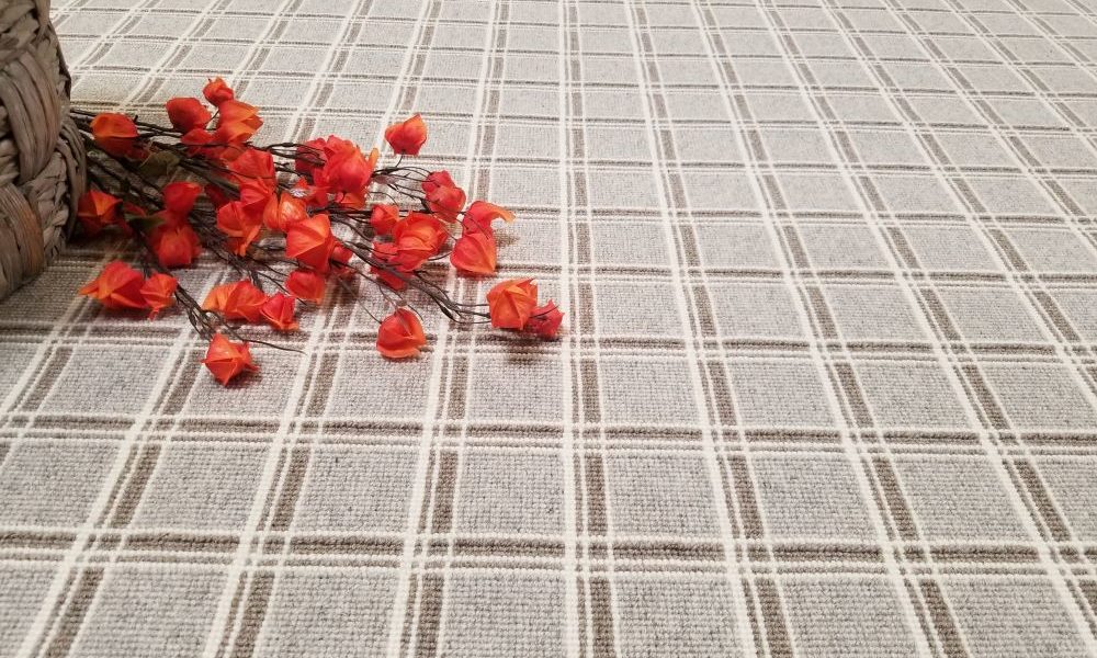 Logan, Color: Gable Grey 29/5766 shown with flowers as prop. Logan is comprised of three different colored yarns (lt taupe, lt grey and natural white) woven across the warp and weft to create a tailored grid design.