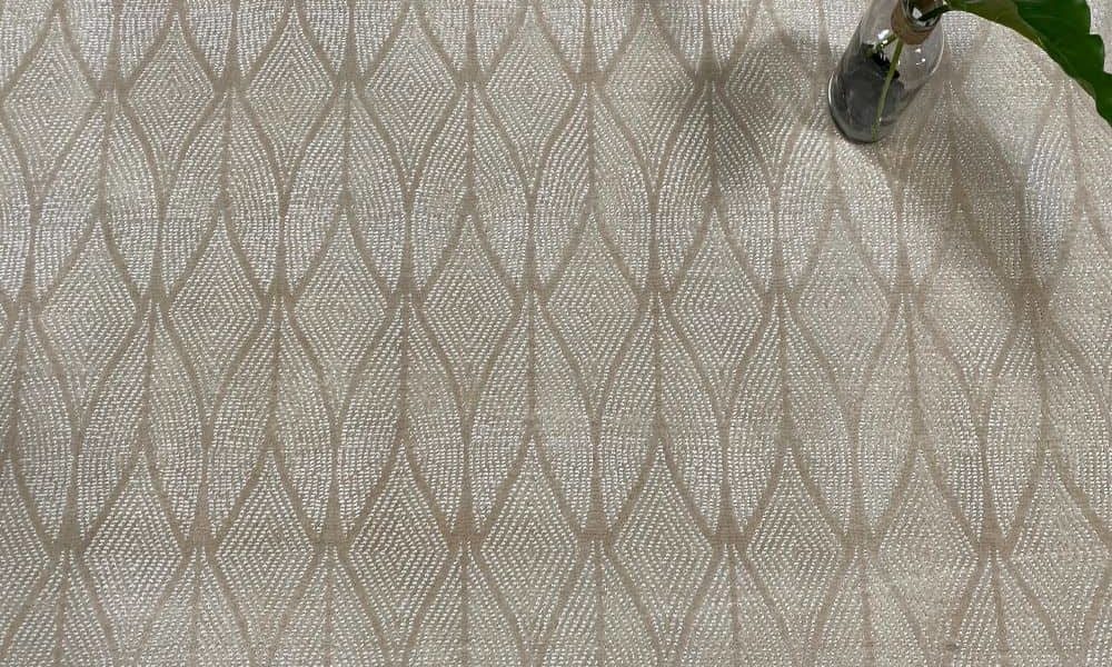 Delano, Color: Beige 1/1601 with plant as prop showing several pattern repeats. Delano is a cut/loop carpet with an Art Deco design motif.
