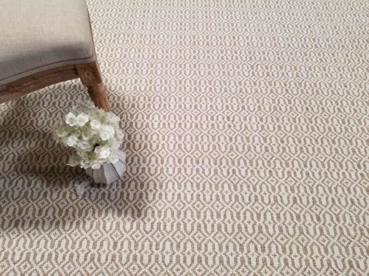 Mosaic, Color: Beige/Ivory 500/1515 shown with chair and flowers as props. Mosaic is a loop pile, hand loomed with 2 yarn colors (beige/white) creating a motif that resemble mosaic tiles.
