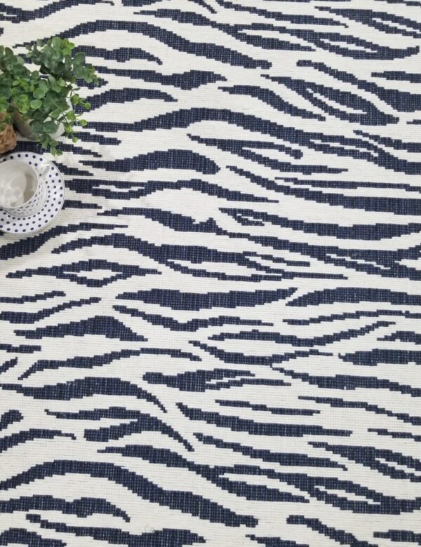 Herne Bay, Color: Navy 790/1544 with props. Herne Bay, Color: Navy 790/1544 with teacup, plant and ottoman used as props. Herne Bay is fabricated with two colors of yarn that creates the animal design.